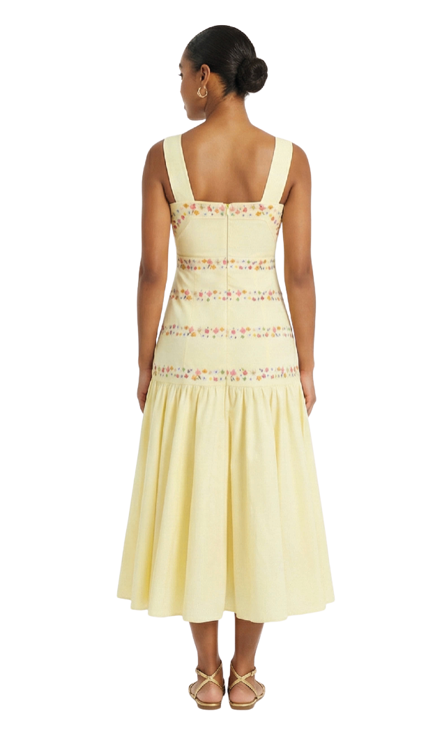 Woman wearing a light yellow dress with floral lace details on a white background