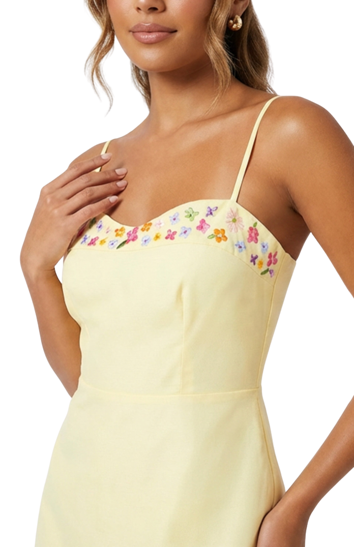 Woman wearing a light yellow dress with floral embroidery on a white background