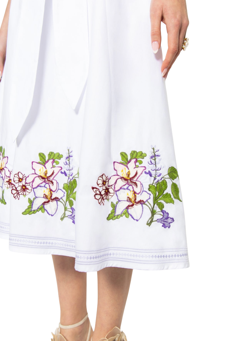 White dress with floral embroidery held by a person on a white background