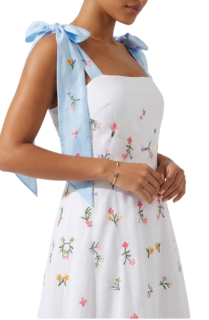 White dress with floral embroidery and a blue ribbon on a white background