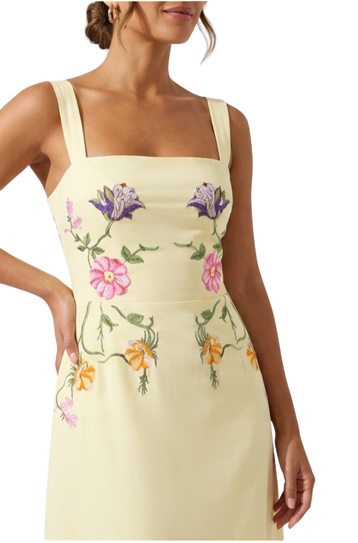 Woman wearing a light yellow dress with floral embroidery on a white background