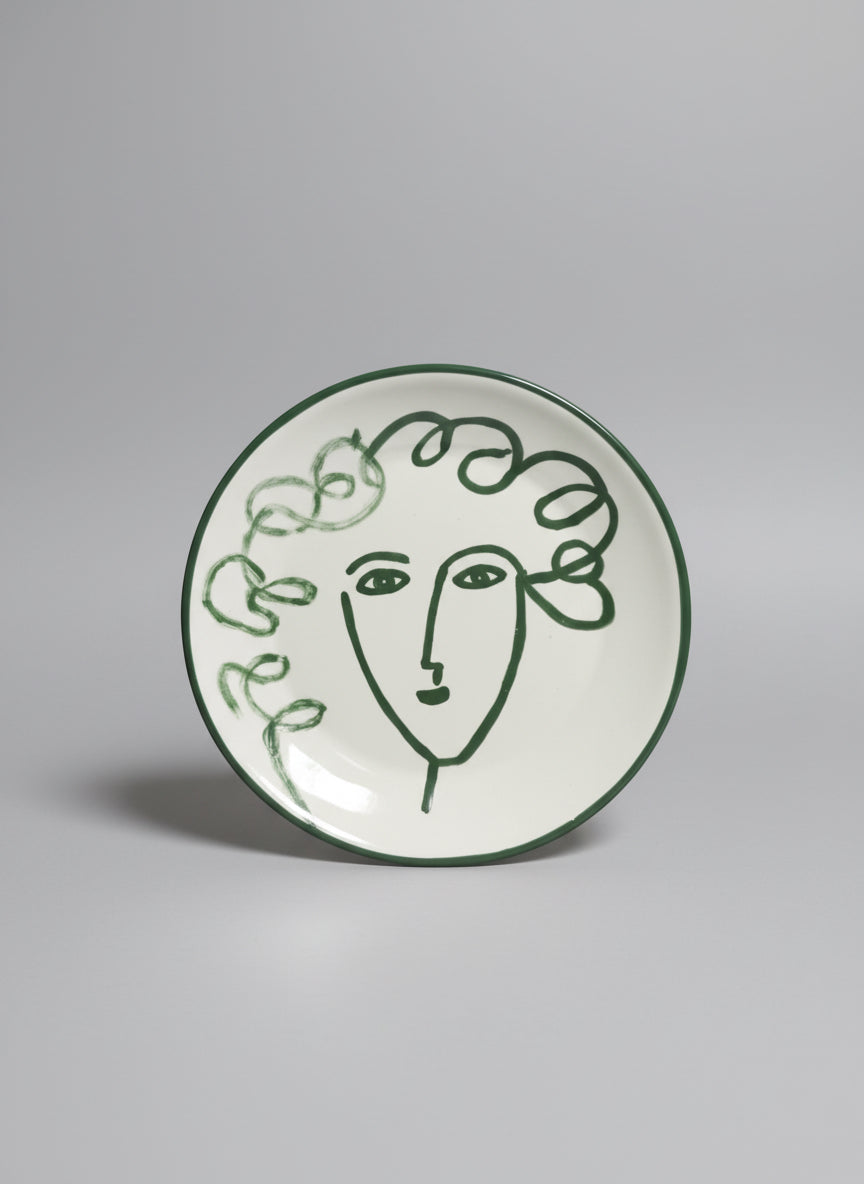 Round ceramic tile with a green line art face design on a white background