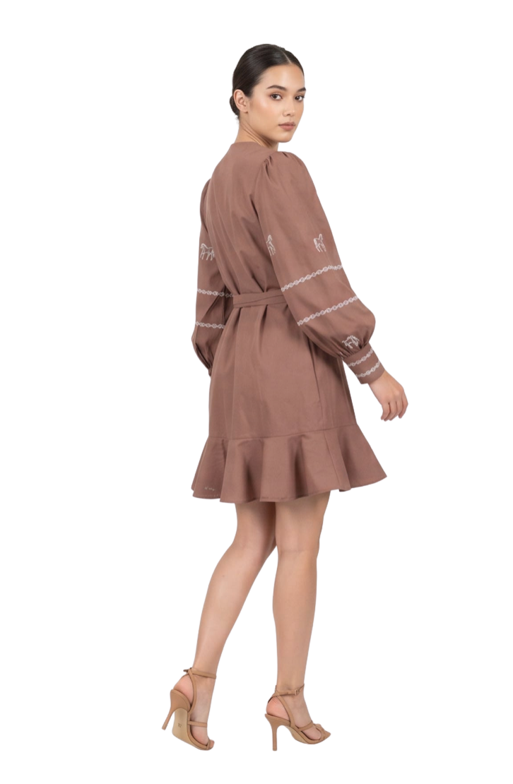 A woman modeling a brown long-sleeve mini dress with white embroidered details on the sleeves, shown from a rear three-quarter angle against a plain white studio background.