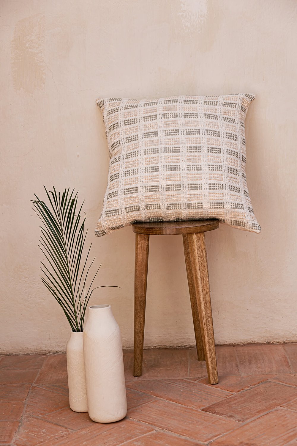 Decorative pillow in two color options: Earth Brown & Cream and Sage Green & Cream. Measuring 50.5 x 50.5 cm (20 x 20 inches), this pillow is made from 100% organic cotton with undyed and naturally dyed handspun and industrially spun yarn. It features a golden metal zipper pull and a plain weave organic cotton back. Handmade by a women artisan cooperative in Charalá, Colombia, this eco-friendly pillow reflects a commitment to zero-waste textile production.