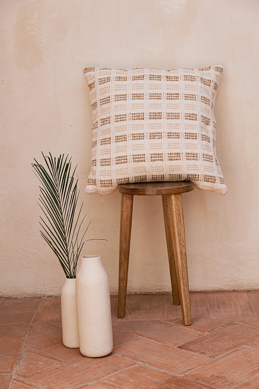 Decorative pillow in two color options: Earth Brown & Cream and Sage Green & Cream. Measuring 50.5 x 50.5 cm (20 x 20 inches), this pillow is made from 100% organic cotton with undyed and naturally dyed handspun and industrially spun yarn. It features a golden metal zipper pull and a plain weave organic cotton back. Handmade by a women artisan cooperative in Charalá, Colombia, this eco-friendly pillow reflects a commitment to zero-waste textile production.