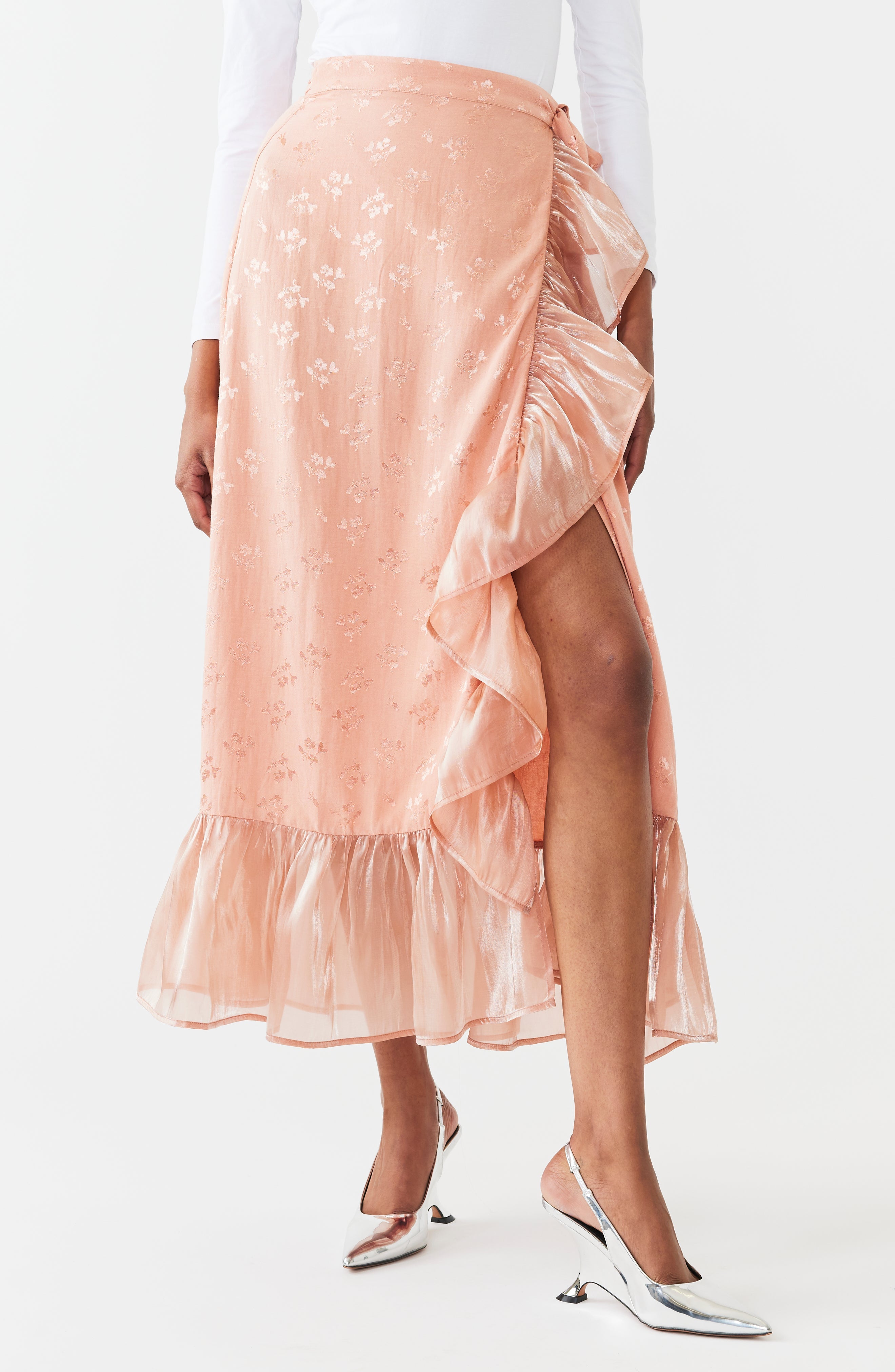 Blush pink embroidered midi wrap skirt with cascading ruffles and asymmetrical hem, shown on model with white top and kitten heels