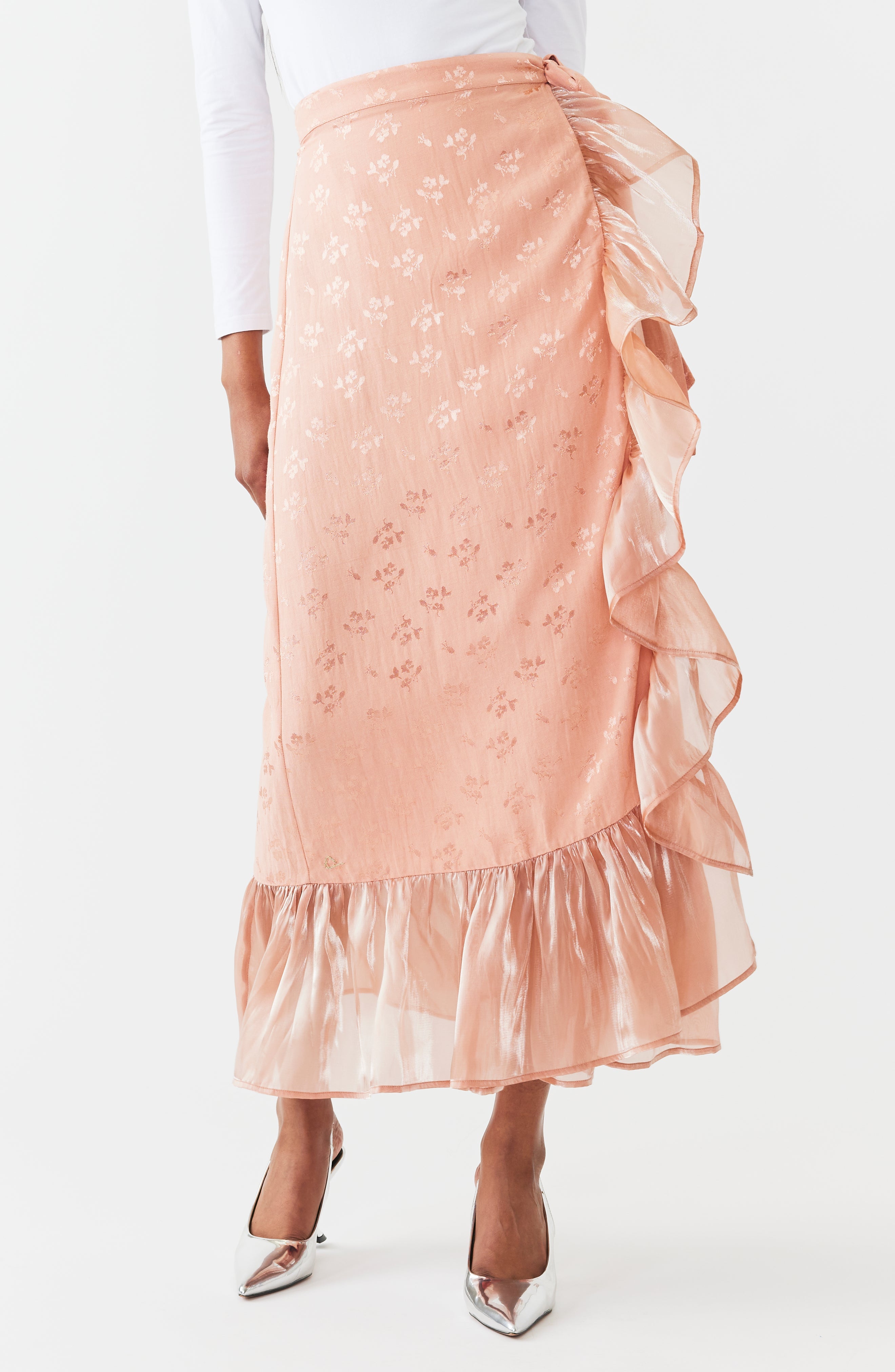 Blush pink embroidered midi wrap skirt with cascading ruffles and asymmetrical hem, shown on model with white top and kitten heels