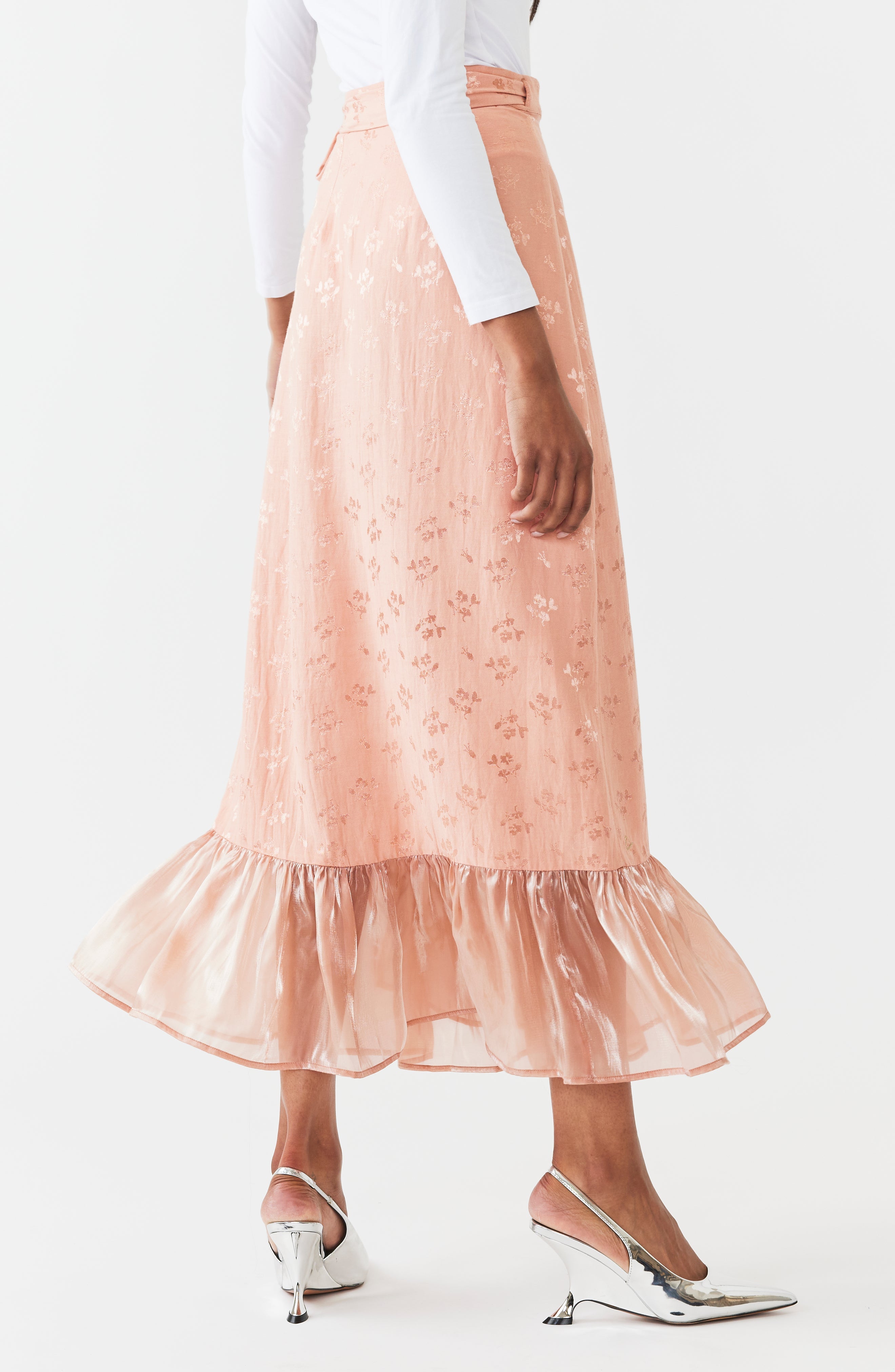 Blush pink embroidered midi wrap skirt with cascading ruffles and asymmetrical hem, shown on model with white top and kitten heels