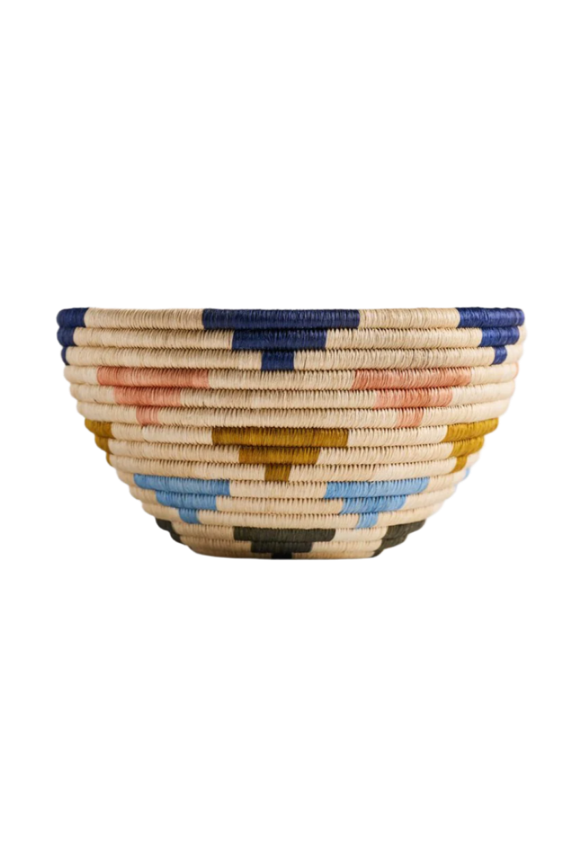 A vibrant fruit bowl featuring a blend of navy blue, cielo blue, salmon pink, olive green, and natural colors. Made from 100% natural fique, this handcrafted piece from Guacamayas, Colombia, adds a lively Caribbean touch to any table or shelf. Dimensions: 15 x 25 cm.