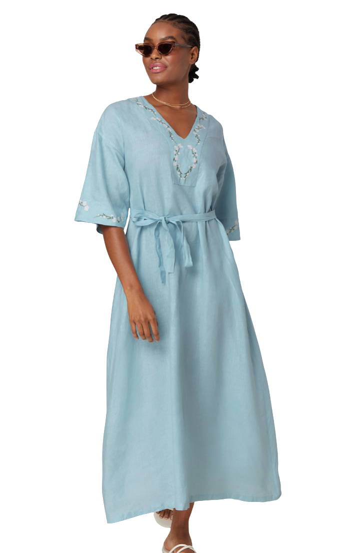 A woman modeling a light blue kaftan dress with embroidered details on the neckline and sleeves, featuring a tie waist belt, set against a plain white background.