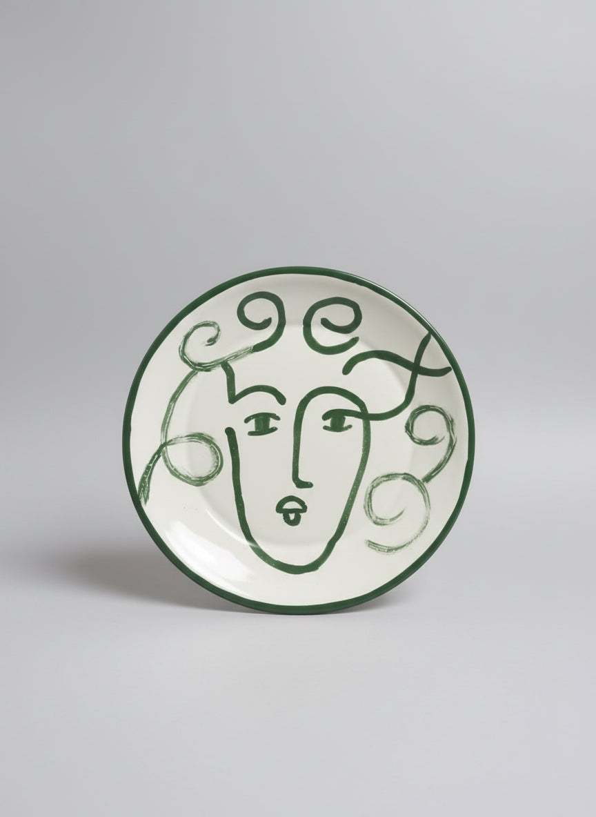 Decorative plate with green line art face design on a white background