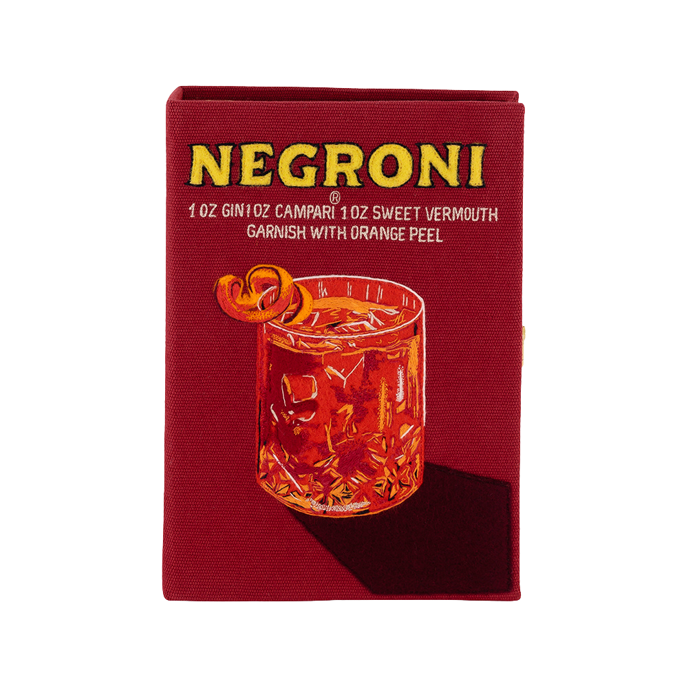 A square red fabric napkin featuring a printed illustration of a Negroni cocktail in a glass, with yellow text reading 'NEGRONI' and smaller white text detailing the ingredients and garnish, set against a plain white background.