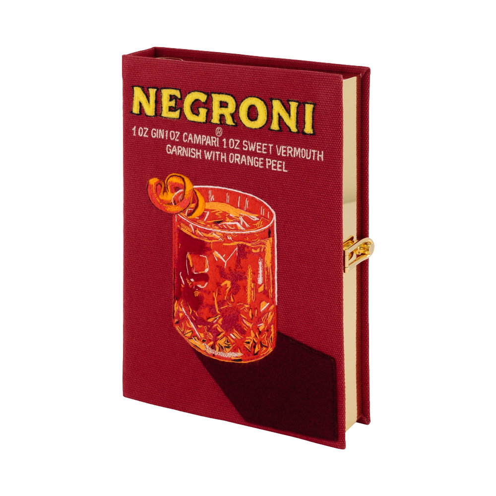 A hardcover notebook or journal styled like a Negroni cocktail package, featuring a deep red cover with yellow 'NEGRONI' text and an illustration of an orange cocktail glass. The notebook is shown open slightly to reveal beige pages and a gold clasp, set against a plain white background.
