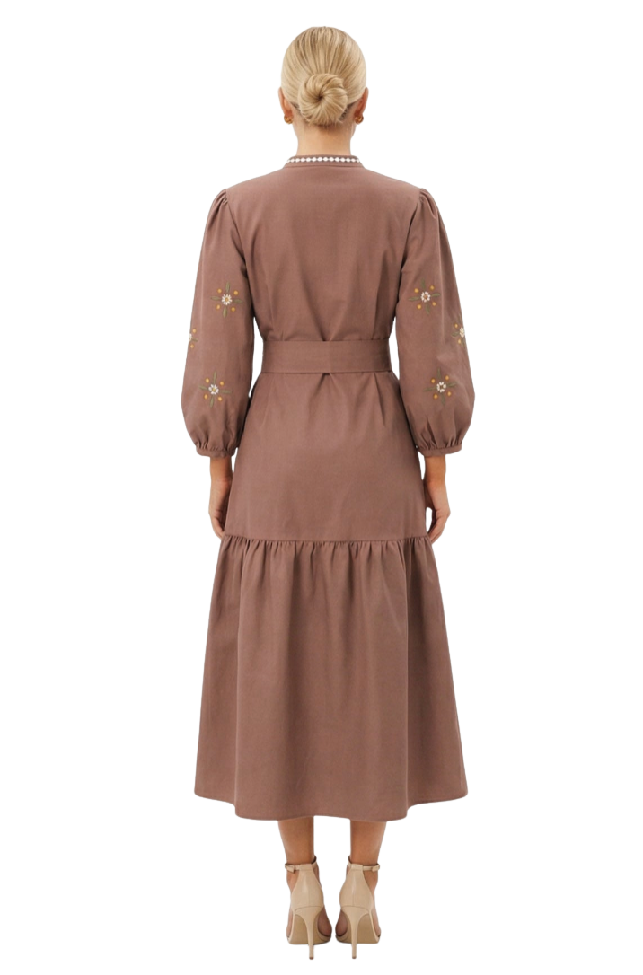 A woman viewed from the back wearing a dusty rose-brown midi dress with long puff sleeves, a matching waist belt, and small embroidered floral details on the sleeves, paired with beige high-heeled sandals against a plain white studio background.