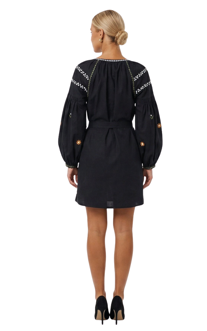 A woman shown from the back wearing a black mini dress with long balloon sleeves, embroidered details on the shoulders and upper arms, and a matching black belt. She is wearing black high heels against a plain white studio background.
