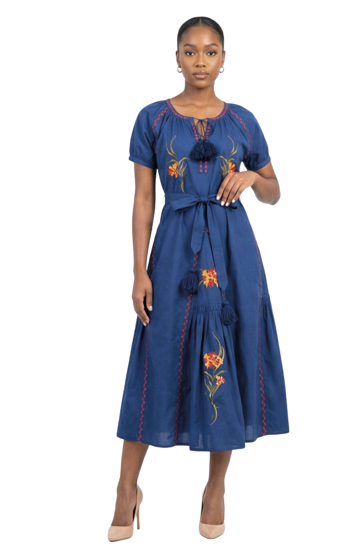 A woman modeling a blue midi dress with short sleeves, a self-tie waist belt, and colorful floral embroidery on a white studio background.