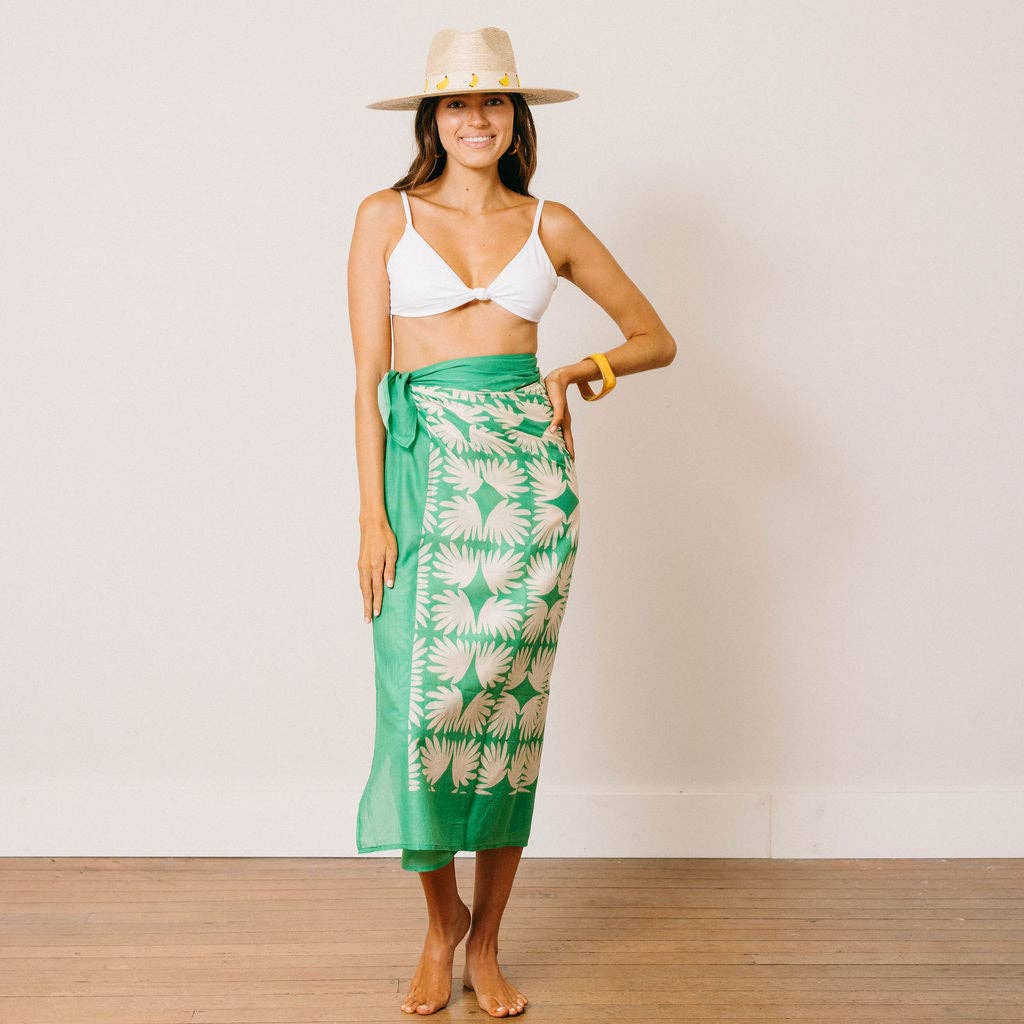 Woman wearing a white bikini top and green patterned sarong against a plain background