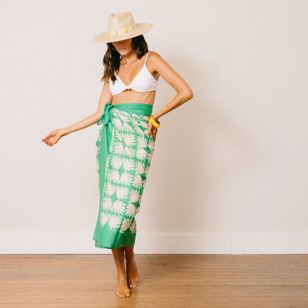 Woman wearing a green floral sarong and white bikini top against a plain background
