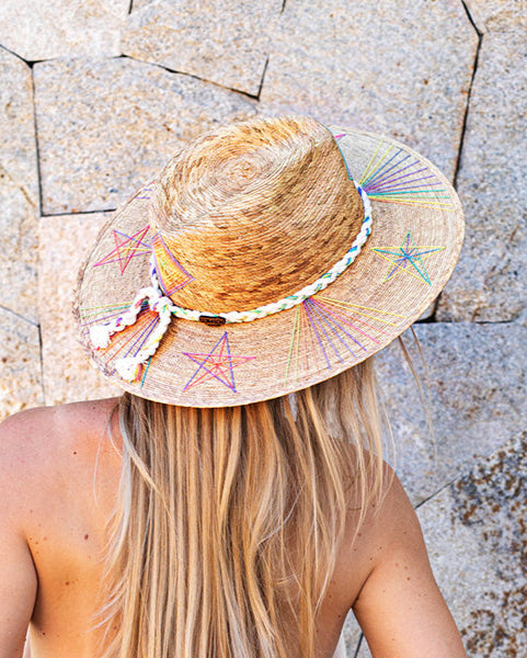 Person wearing a straw hat with star patterns against a stone wall background