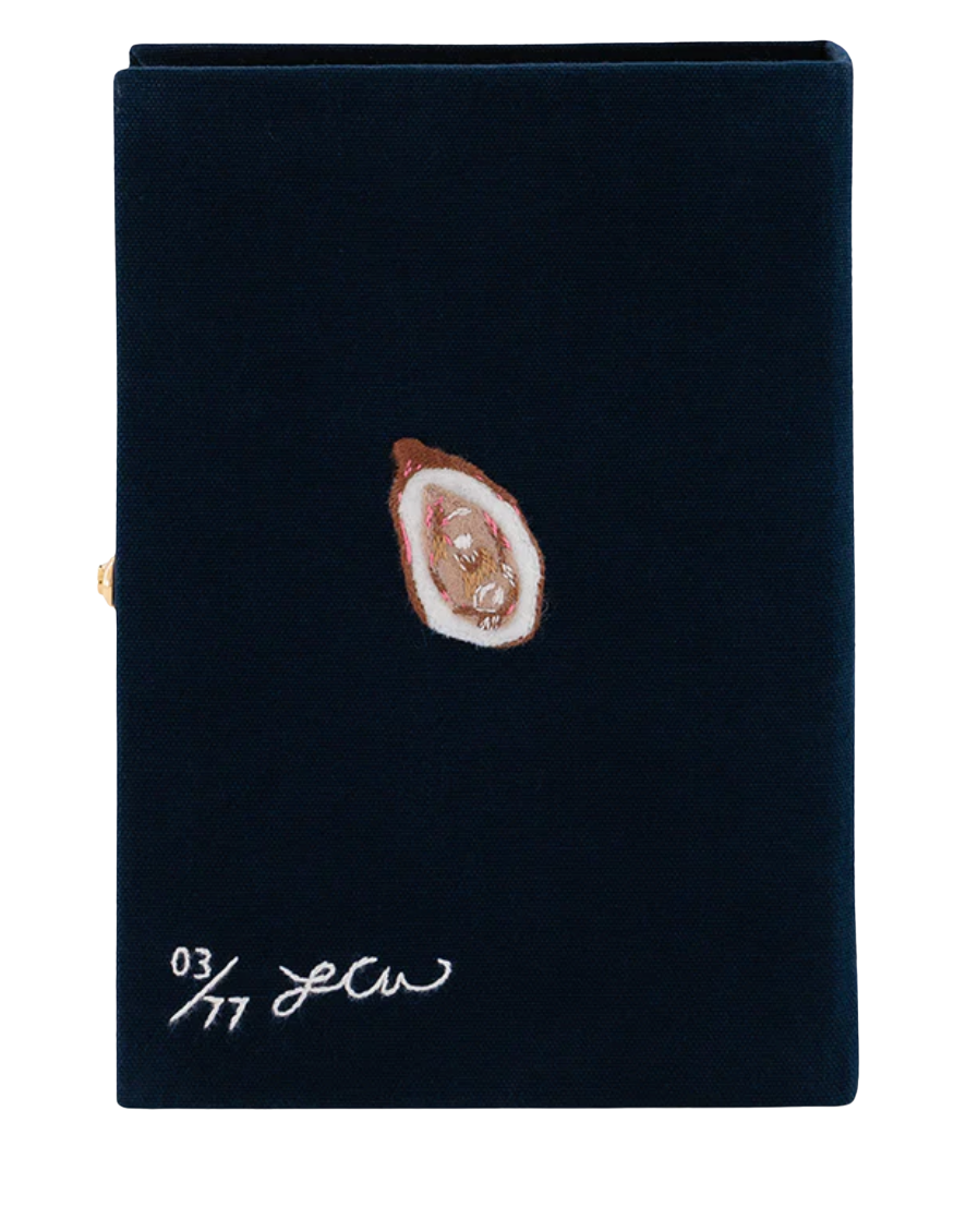 A dark navy blue velvet notebook or journal cover with a small oyster shell illustration and white script text near the bottom, shown on a plain white background.
