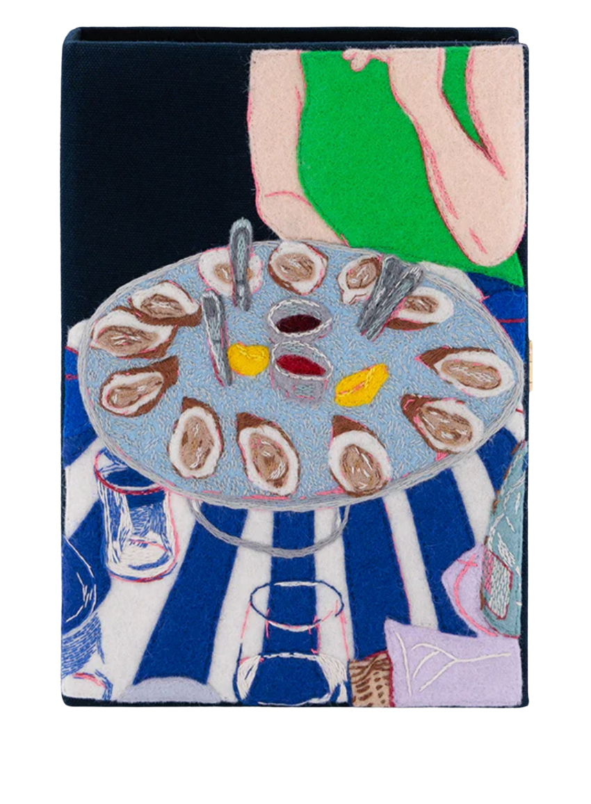 A square textile product, likely a bag or pouch, featuring a colorful embroidered or printed illustration of a table setting with oysters, glasses, and a person in a green top against a dark background.