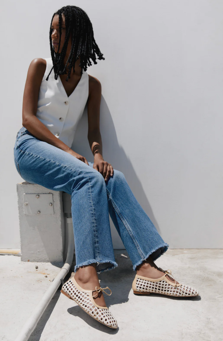 Person wearing blue jeans and white top sitting on a concrete block against a white wall.